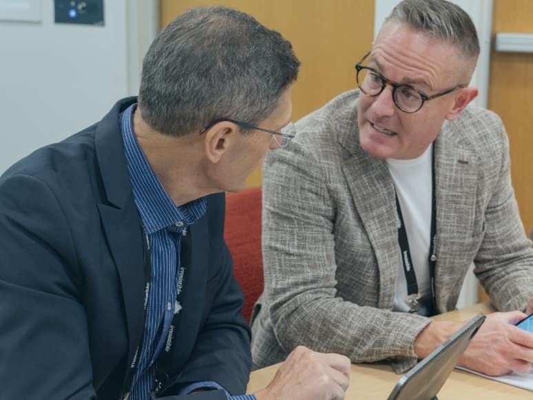 two people sitting at a table looking at a laptop
